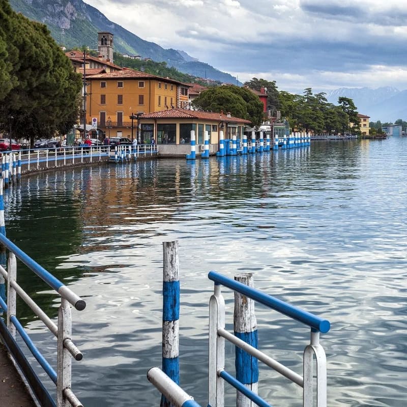 il lungolago con i pali blu e bianchi dell'imbarcadero e i palazzi affacciati sull'acqua