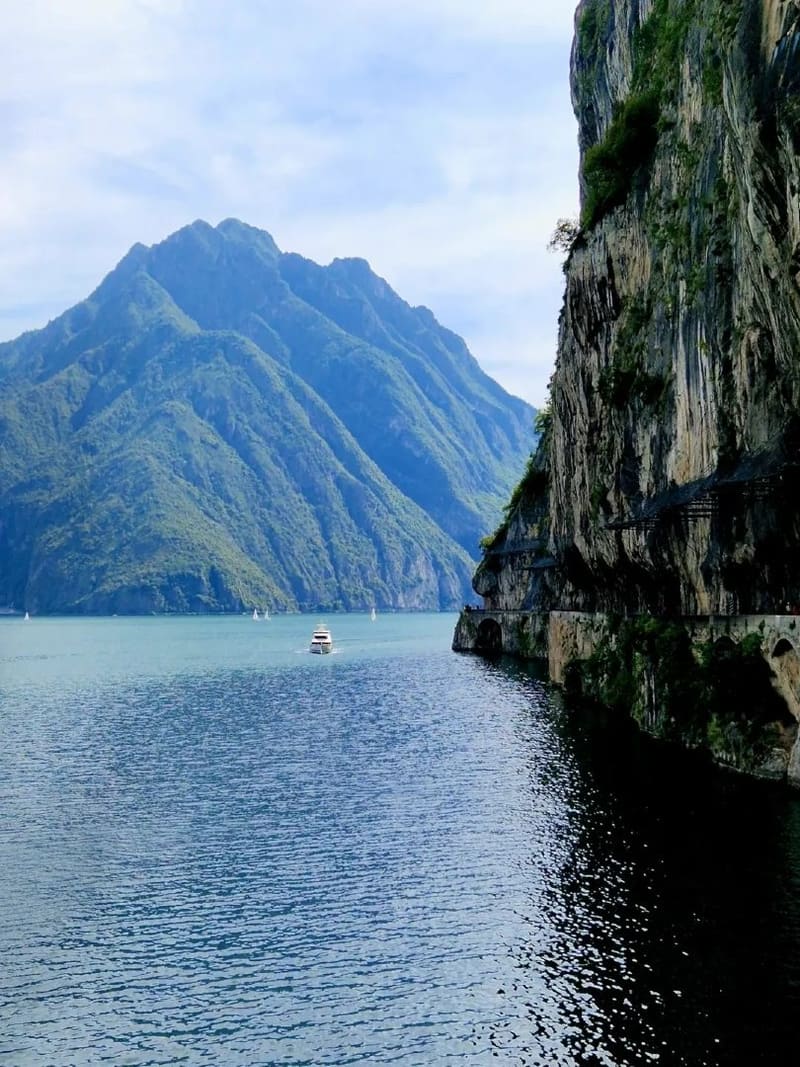 le pareti a picco sul lago con il camminamento scavato nella roccia e un battello in navigazione