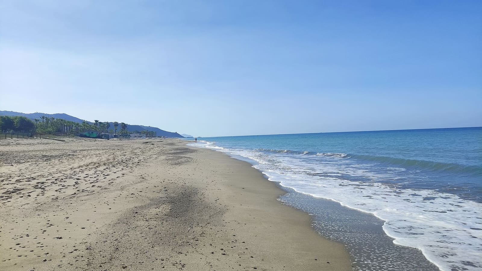 der leere Strand, mit den Wellen und hinten der Küste