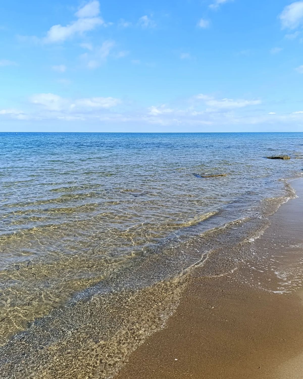 l'acqua trasparente che si stende sulla battigia, con il fondo di sabbia e roccia