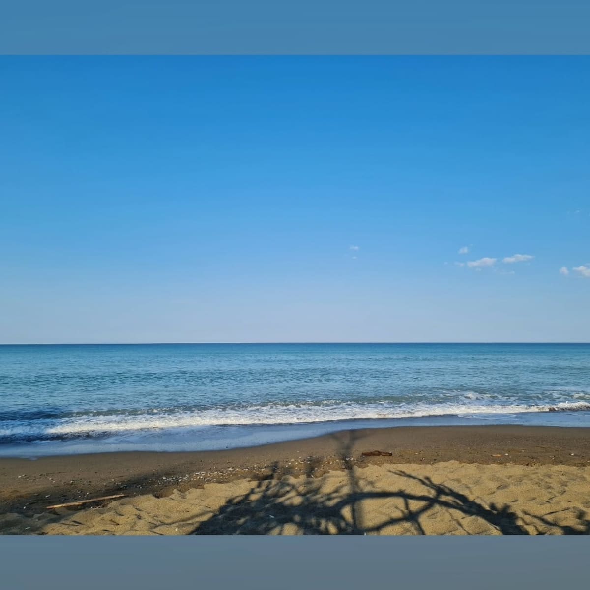 il mare piatto del mattino presto, con l'ombra di una tamerice sulla sabbia
