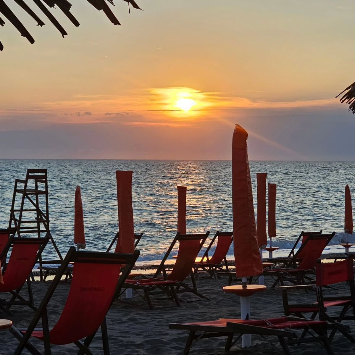 il sole che scende fra gli ombrelloni chiusi e le sdraio dello stabilimento