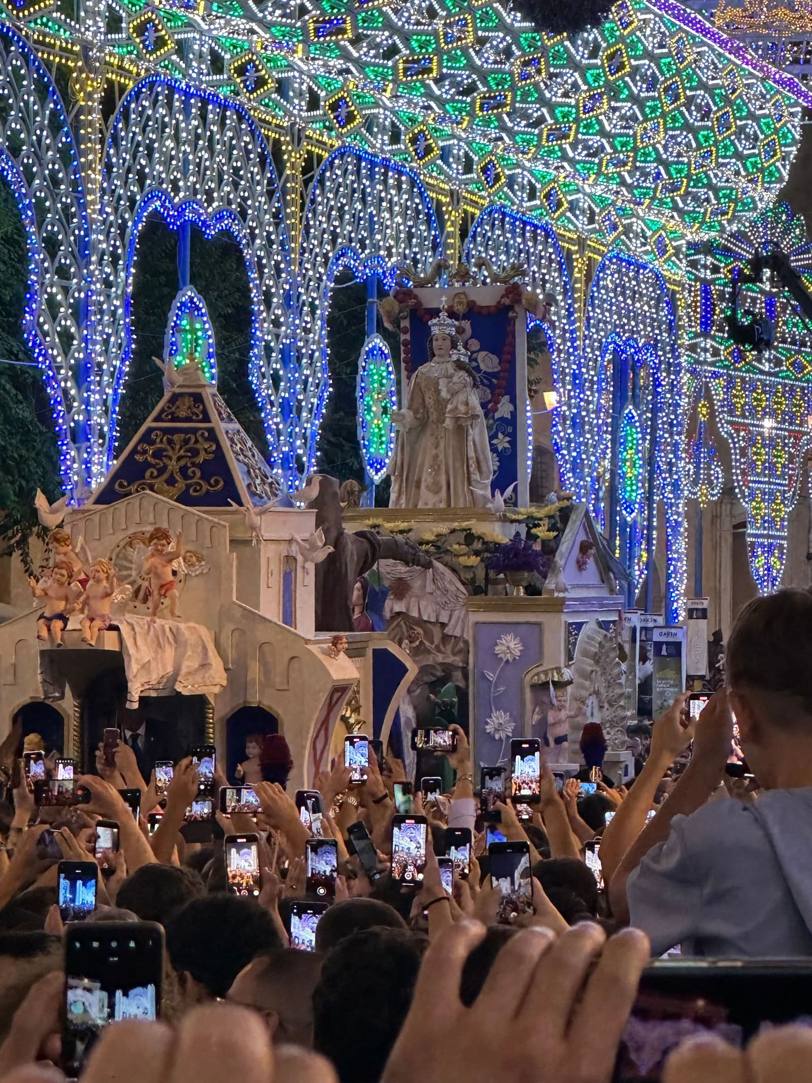 la Madonna della Bruna fra le luminarie, la sera della festa, con i telefoni alzati della folla