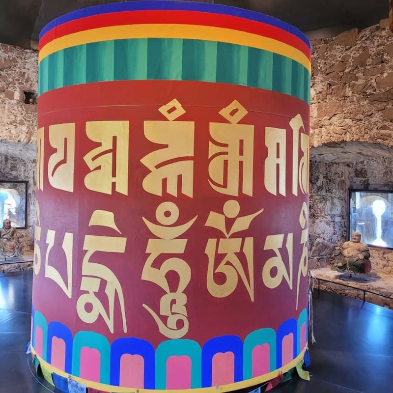 il grande mulino di preghiera tibetano nella sala di pietra, con i Buddha nelle nicchie delle finestre