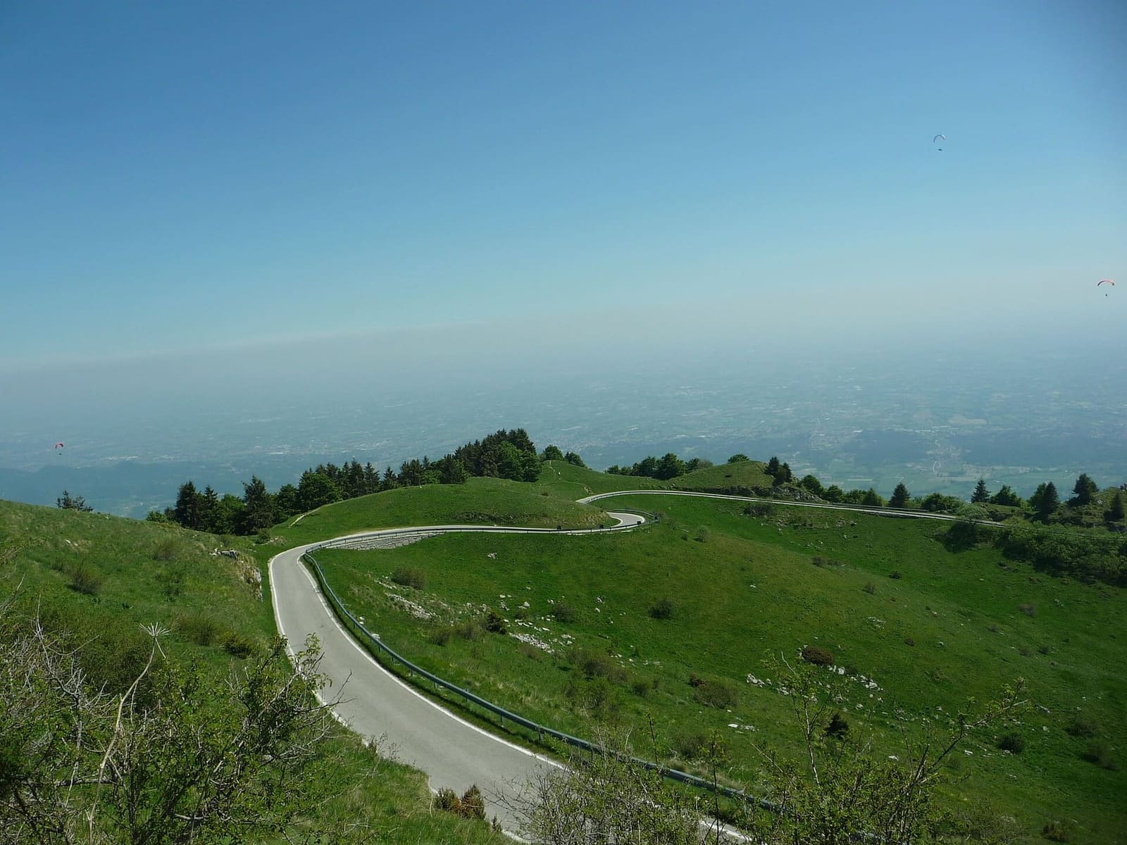 le curve della strada che sale da Semonzo fra i pascoli alti, con i parapendii sopra la pianura