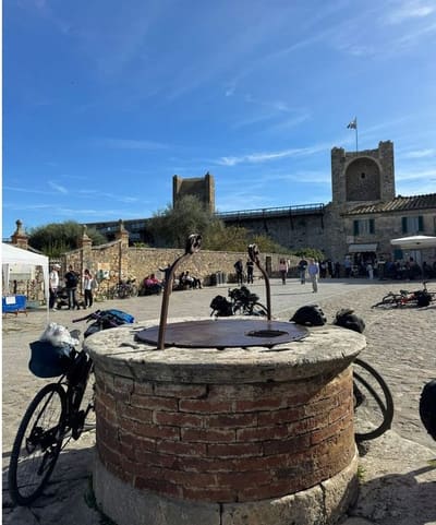 il pozzo di pietra al centro della piazza, con due torri e il camminamento sullo sfondo