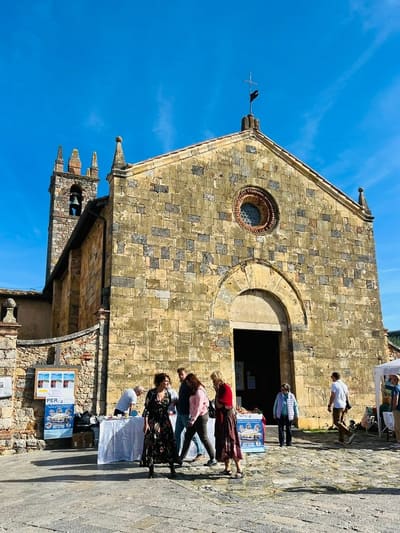 la facciata romanica della pieve e il campanile a vela, con i banchi di un mercatino davanti