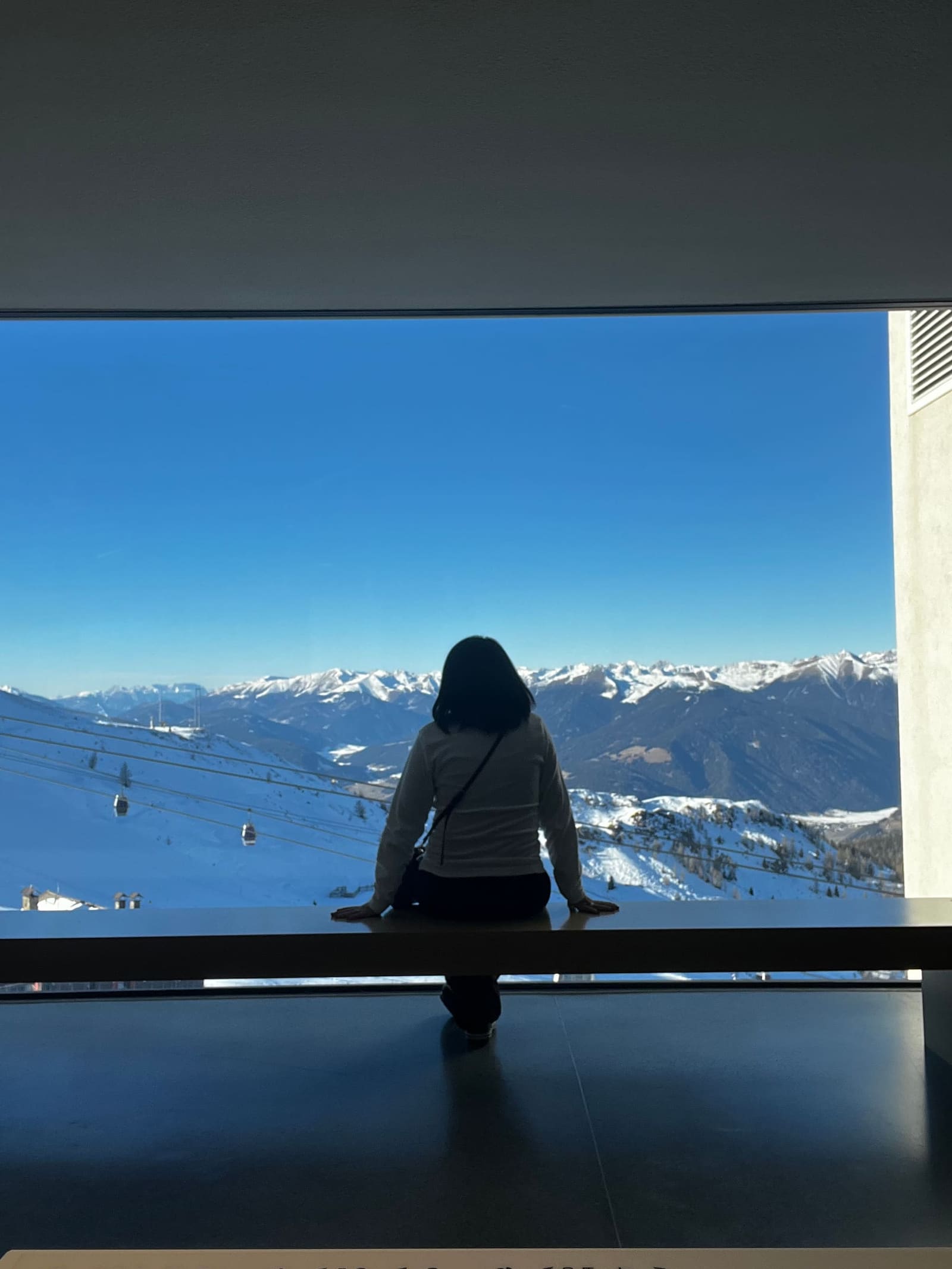 Marcella di spalle alla vetrata, e sotto le piste e le cabine del Plan de Corones