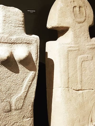 due statue stele della Lunigiana nella sala buia del castello, il cartellino Minucciano III fra le due