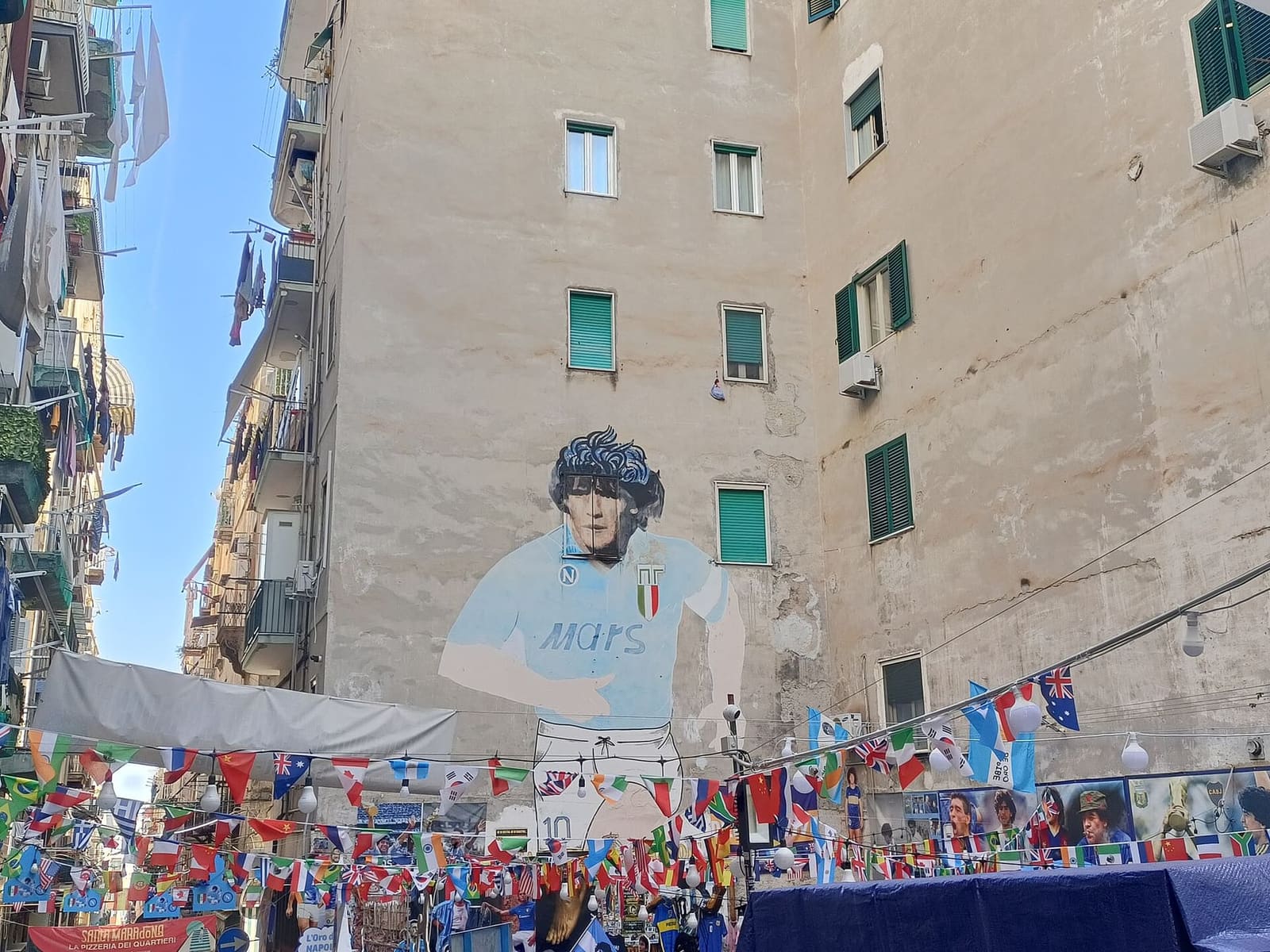 il murale di Maradona con la maglia del Napoli a largo Maradona, sopra le bandierine