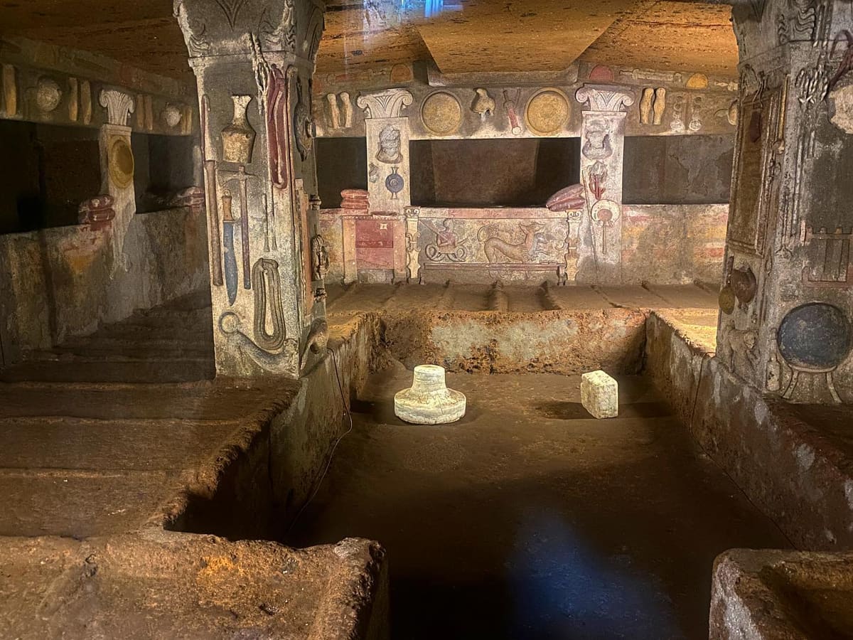 dentro la tomba dei Rilievi: i letti scavati nella roccia e, sui pilastri e sulle pareti, gli attrezzi di casa modellati a stucco e dipinti, con Cerbero a tre teste sul fondo