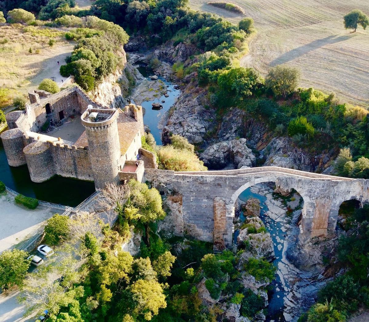 il castello dell'Abbadia e il ponte dell'Abbadia dall'alto: si capisce in un colpo come stanno le cose, il castello con il suo fossato su un lato della gola e il ponte che la scavalca con l'arcata grande, mentre il Fiora d'estate si riduce a un filo fra le rocce