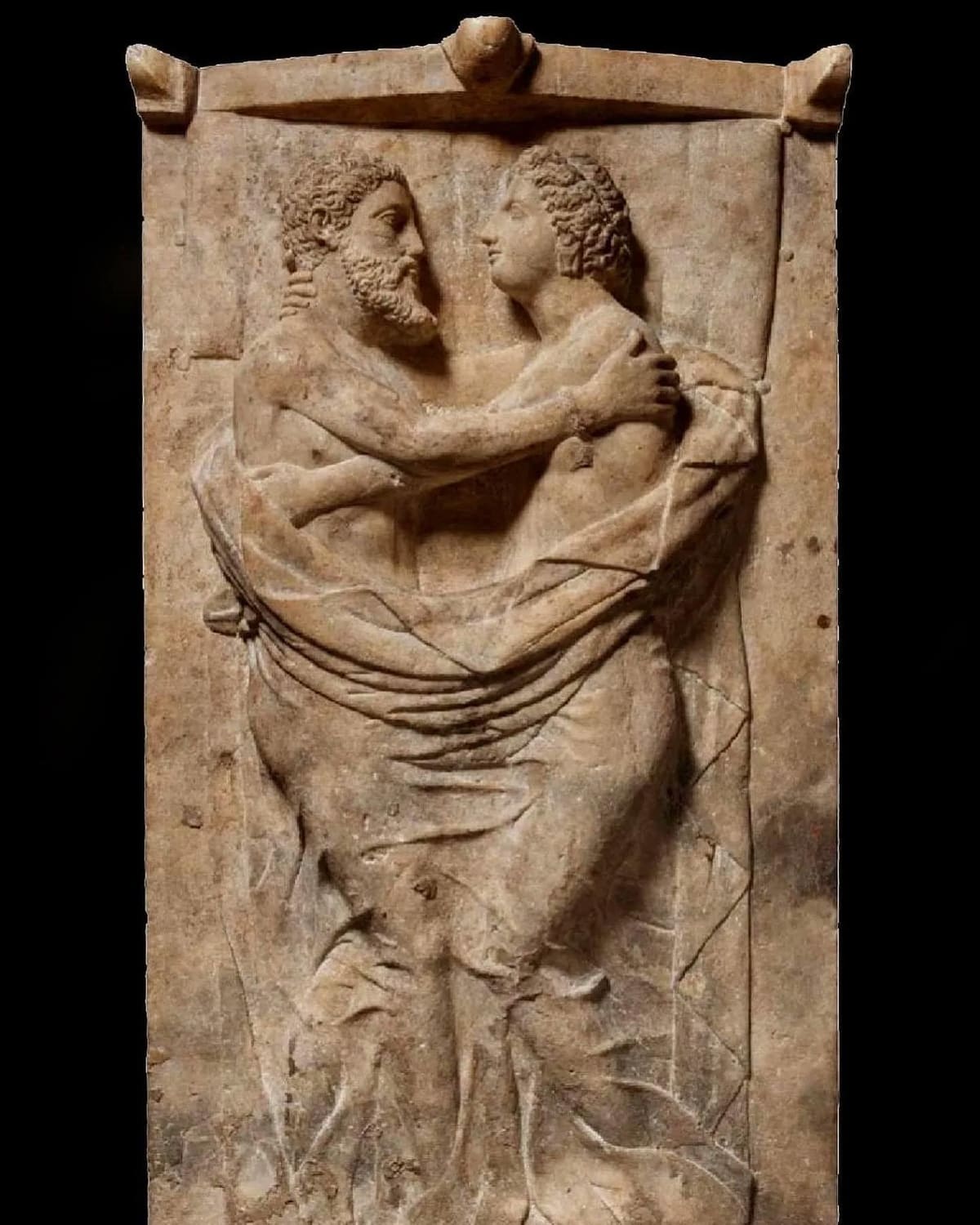 una stele funeraria di marmo: un uomo barbuto e una donna si abbracciano e si guardano, dentro una cornice con gli acroteri sul frontone