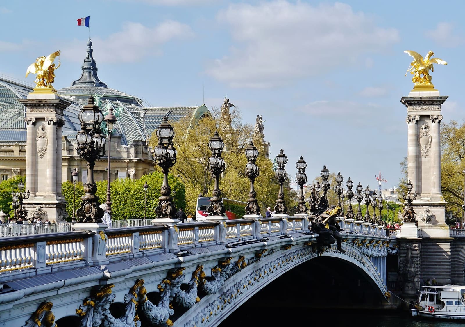 der Pont Alexandre-III mit den Laternen und den vergoldeten Figuren auf den Säulen, dahinter die Kuppel des Grand Palais
