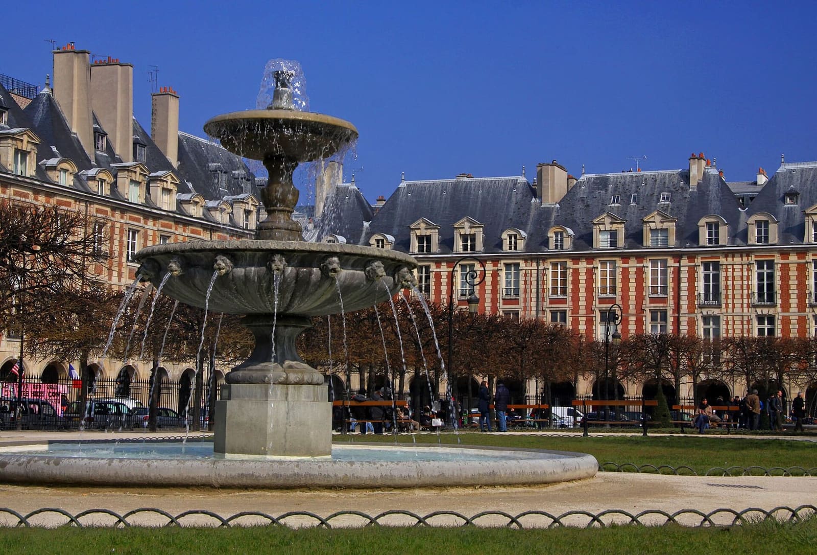 ein Brunnen der Place des Vosges vor den Pavillons aus Backstein und Naturstein