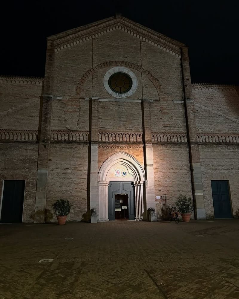 la facciata in mattoni della cattedrale di notte, con il rosone e il portale gotico in marmo