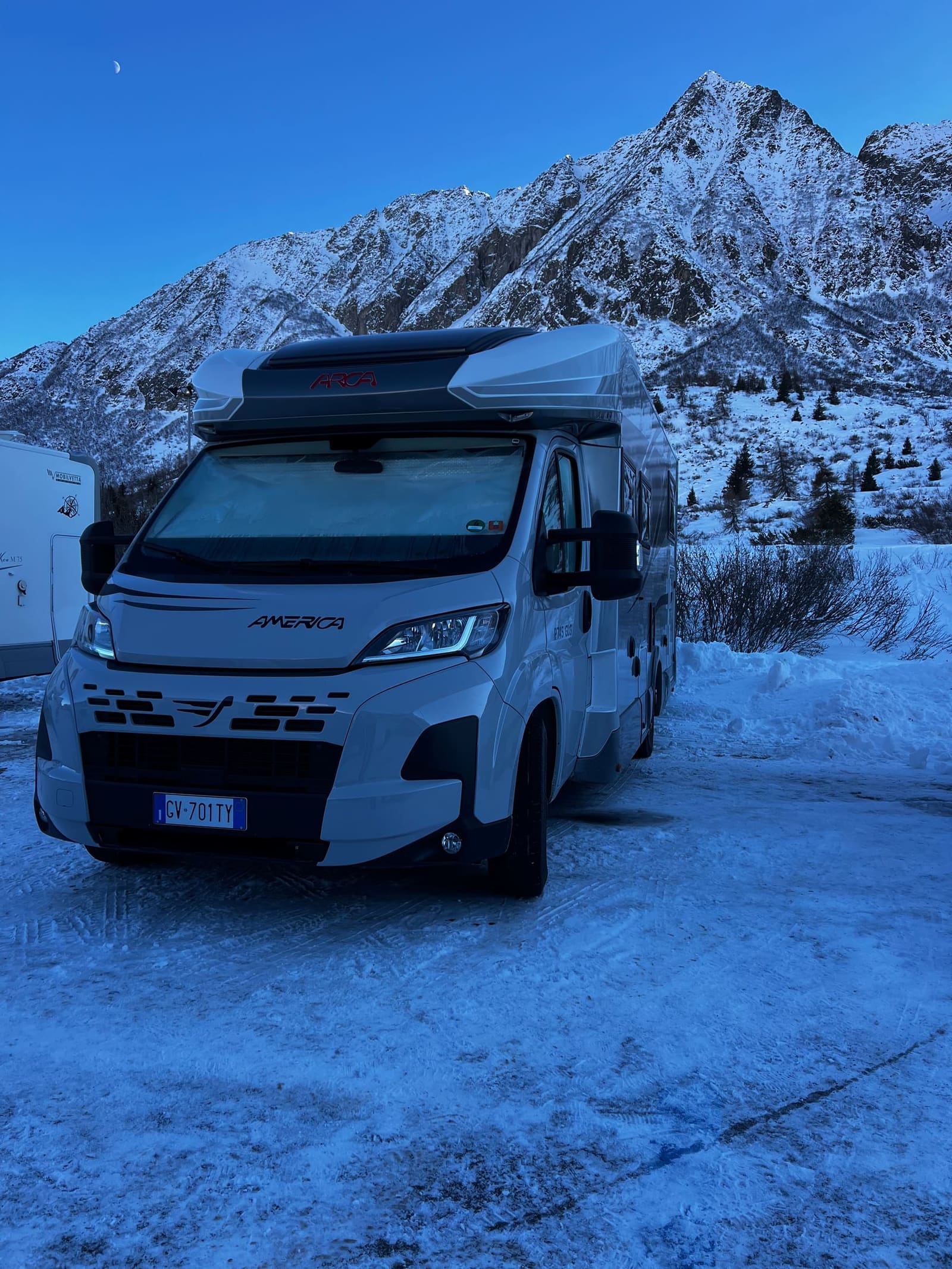 il nostro camper parcheggiato sulla neve al crepuscolo, con la luna sopra la cima