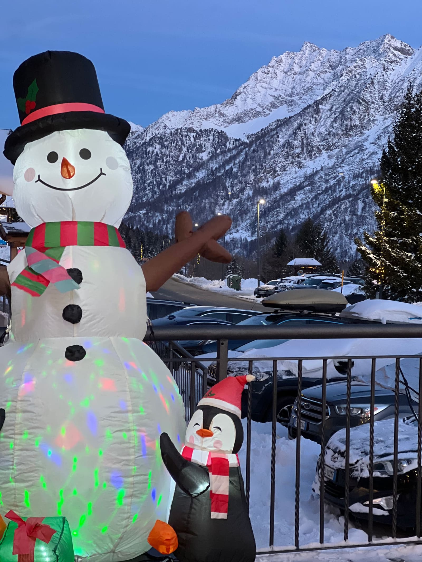 il pupazzo di neve gonfiabile e il pinguino accesi al crepuscolo, sopra il parcheggio innevato