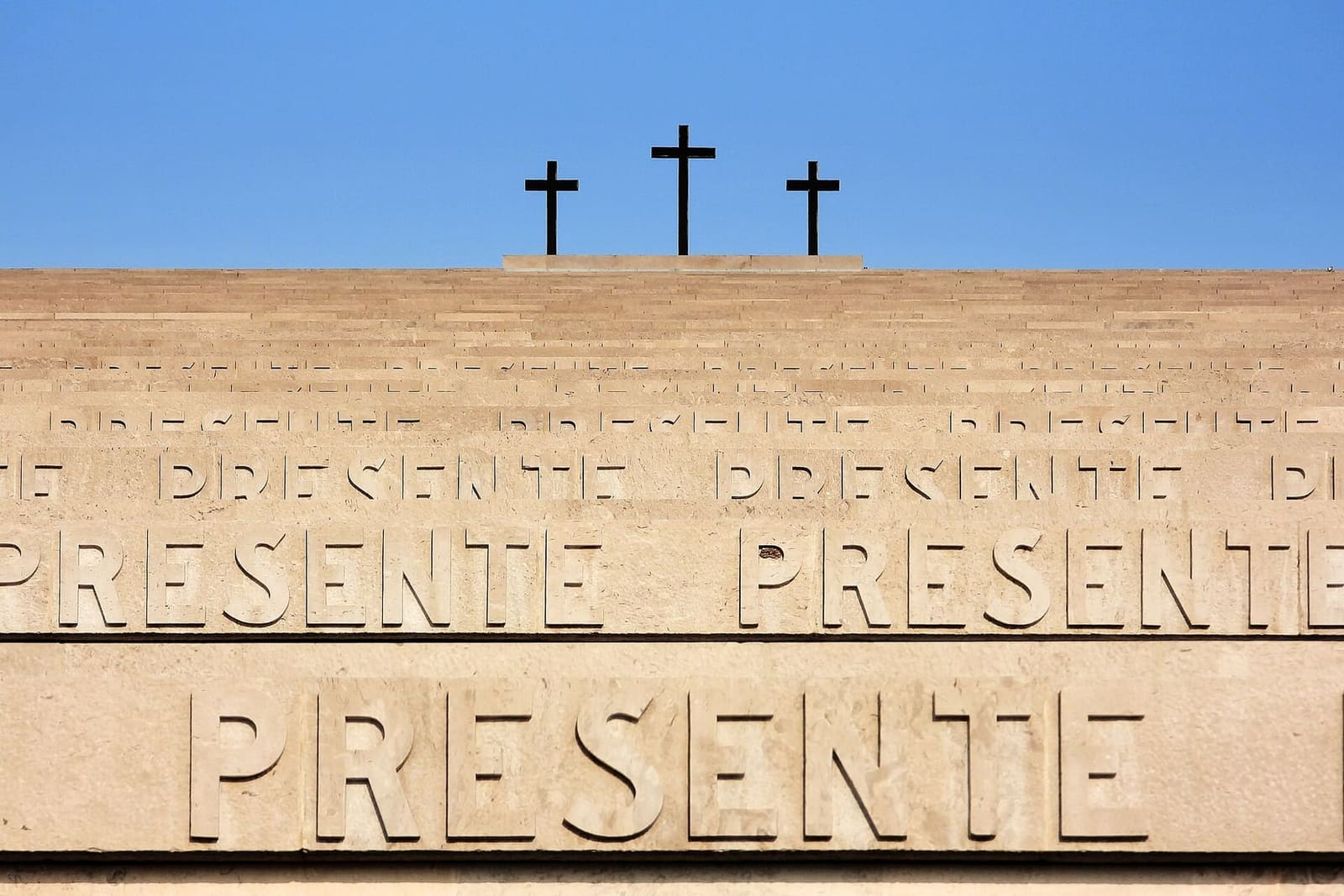 la parola PRESENTE sui gradoni, con le tre croci della cima