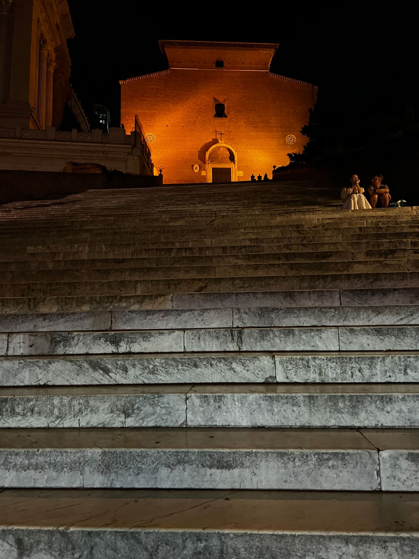 i centoventiquattro gradini dell'Aracoeli visti dal basso, e in cima la facciata di mattoni della basilica illuminata di arancione