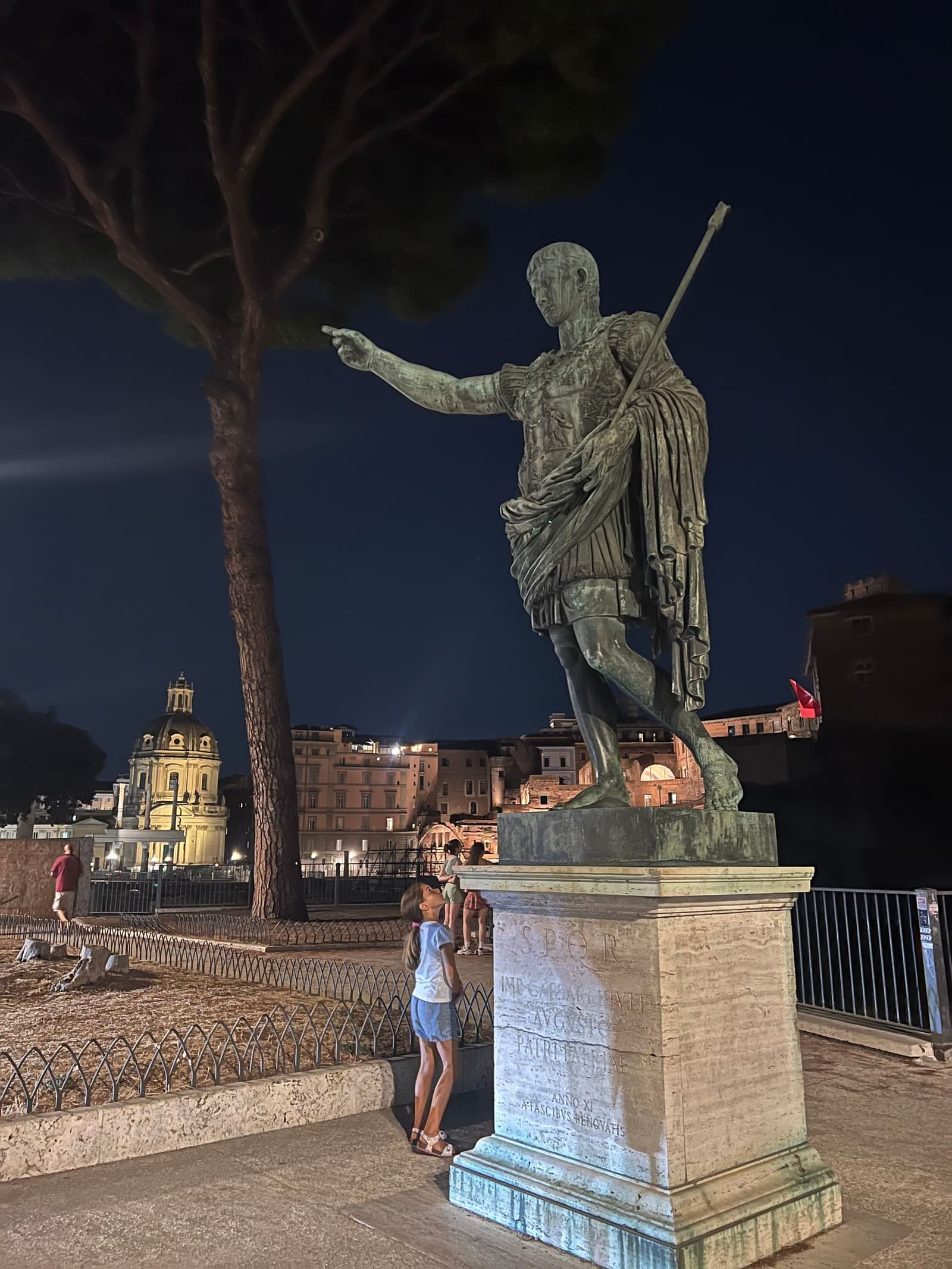 la statua di Augusto con il braccio alzato sulla via dei Fori Imperiali, e Letizia in piedi accanto al basamento che ne dà la misura