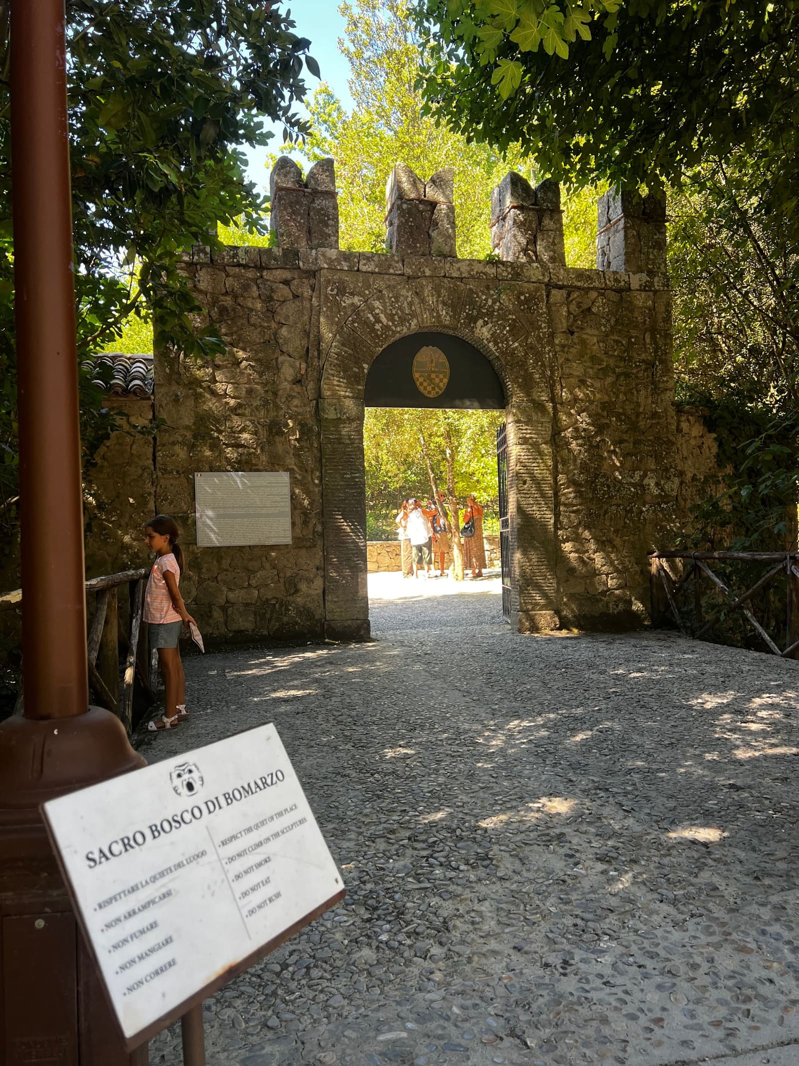il cancello merlato dell'ingresso, e in primo piano il cartello con le regole del bosco: non arrampicarsi, non correre, rispettare la quiete del luogo