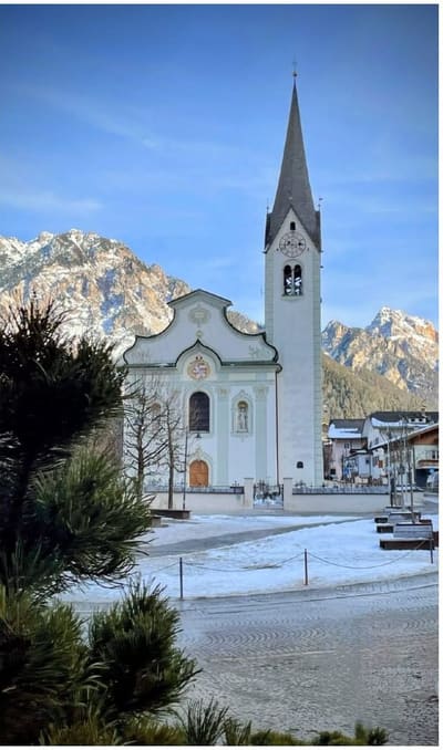la chiesa parrocchiale con il campanile a punta e le Dolomiti alle spalle