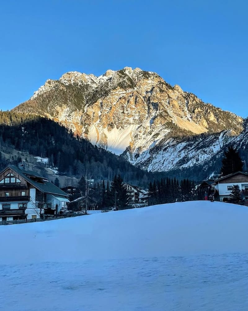 la cima rocciosa illuminata dal primo sole sopra le case e il prato innevato