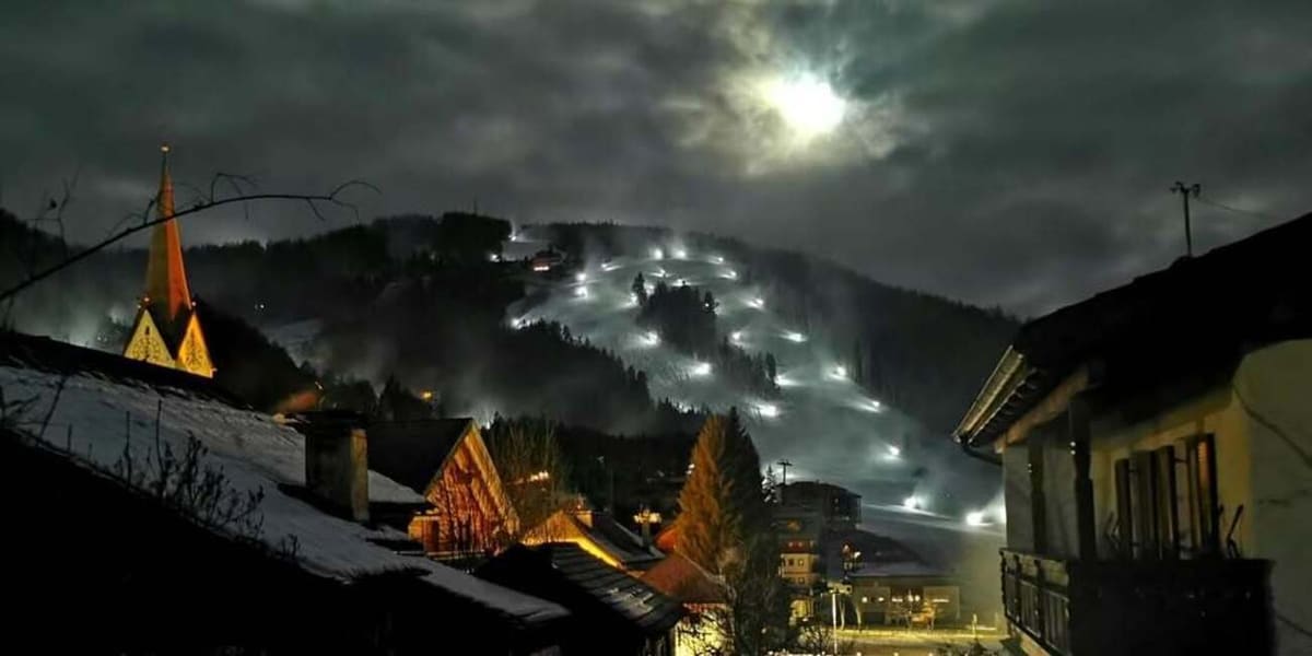il paese di notte, il campanile illuminato e le piste innevate sotto la luna