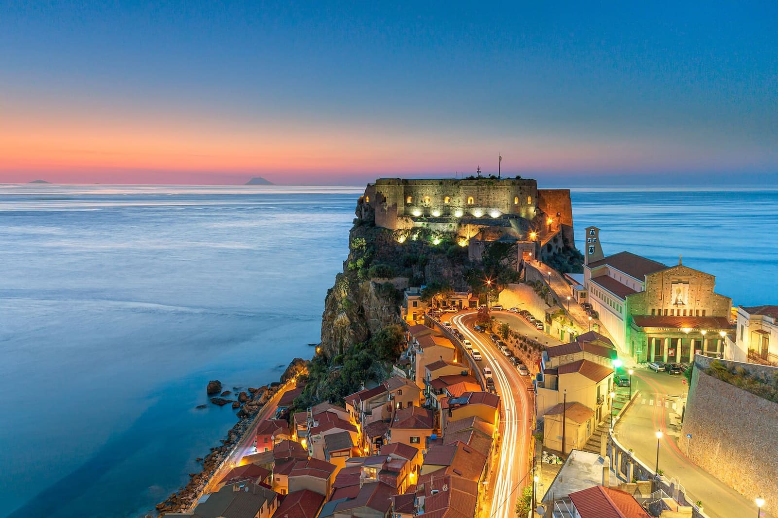 the Castello Ruffo lit up in the evening, with the lights of the village and the sea