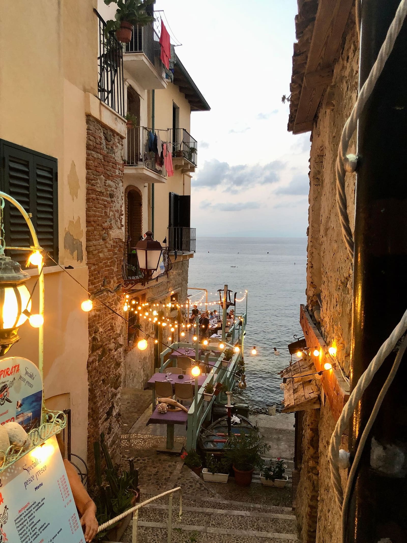 an alley of Chianalea in the evening, with the lights on and the sea at the end