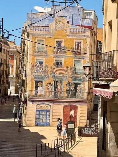 la facciata dipinta a trompe l'oeil che chiude Plaça dels Sedassos, con balconi e personaggi finti