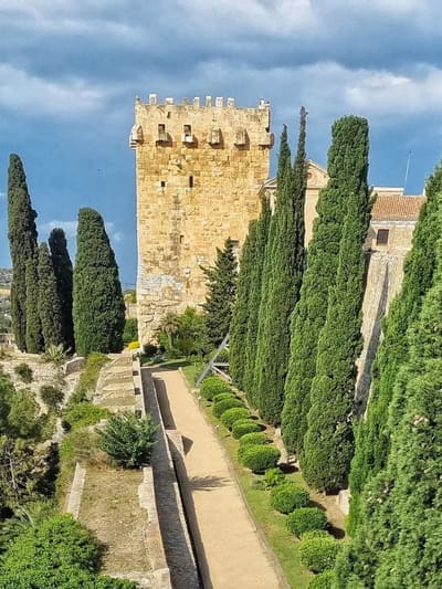 una torre merlata delle mura romane e il vialetto fra i cipressi che le corre accanto