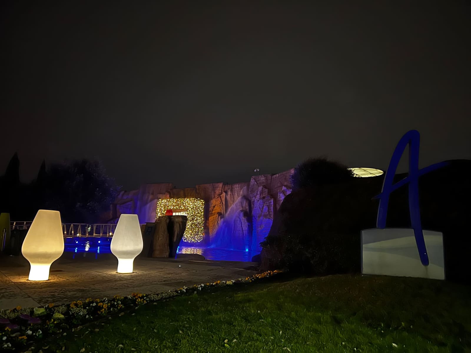 il parco termale di notte, la parete di roccia illuminata di blu e la cascata di luci, con la A dell'insegna