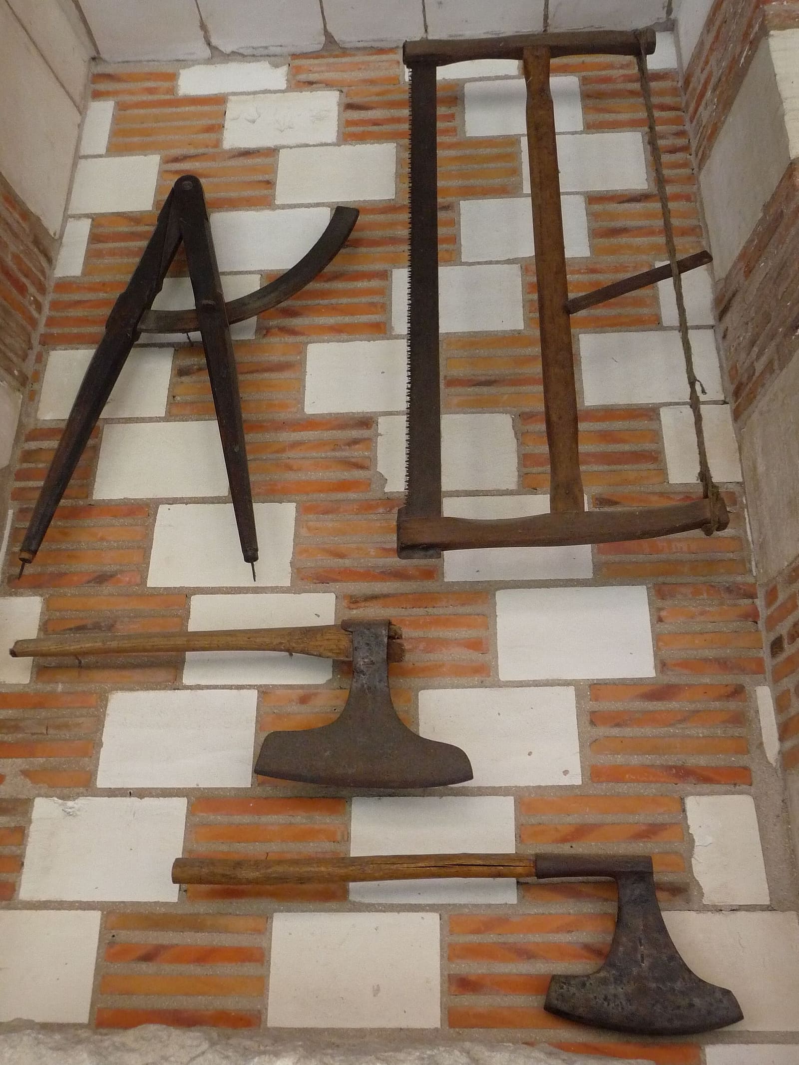 un compasso, una sega e due asce appesi al muro a scacchi di mattoni e pietra bianca dell'hôtel de Mauroy