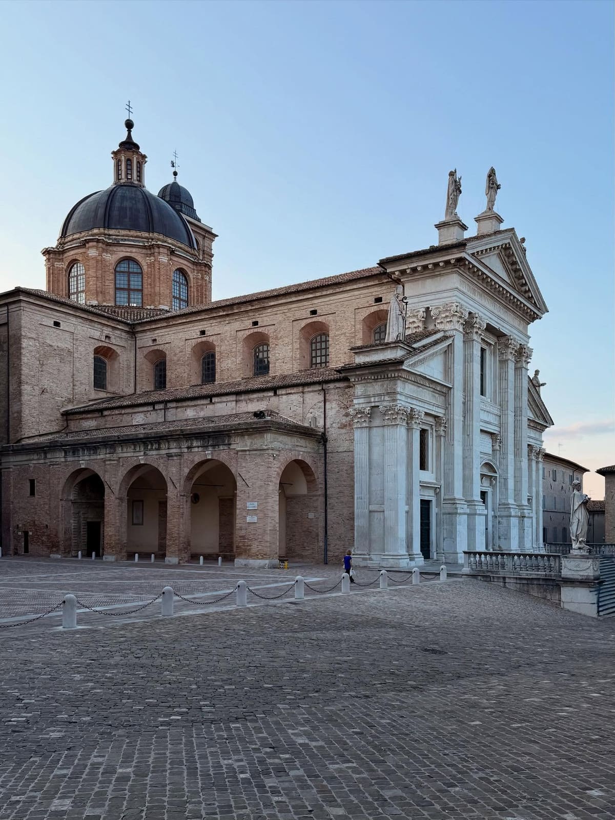 il duomo con la cupola nera e la facciata di pietra chiara, all'alba, con la piazza acciottolata vuota davanti