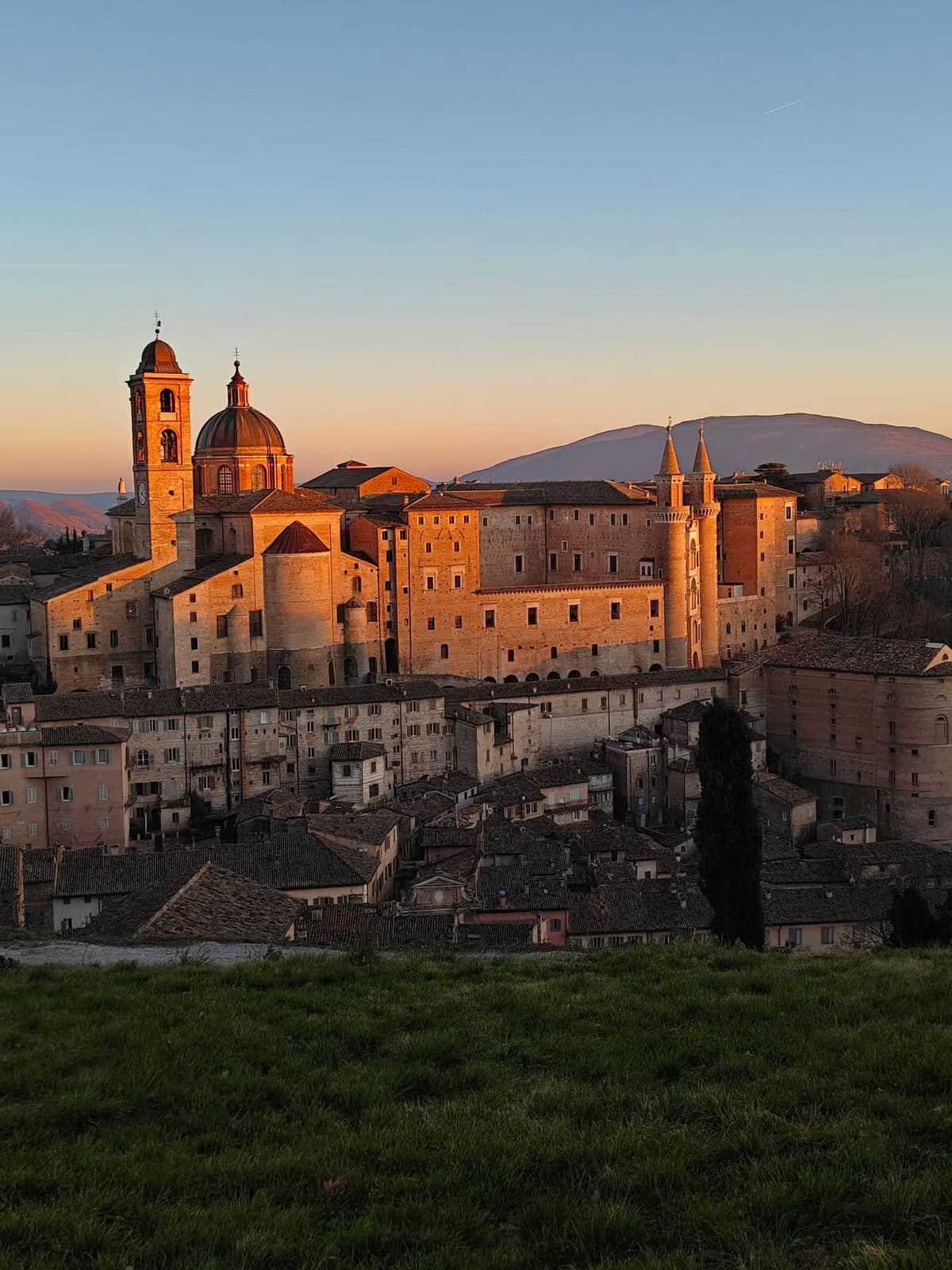 la città intera al tramonto, con il palazzo e i due torricini presi dall'ultima luce e il campanile del duomo accanto