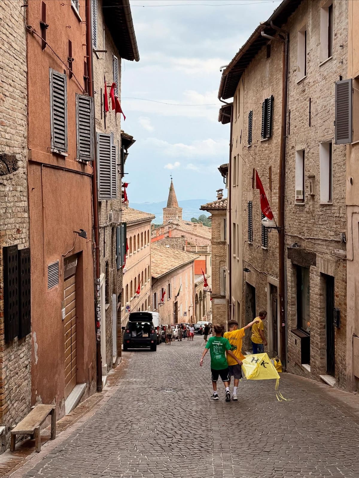 la via in discesa fra le case, con le bandiere rosse appese ai muri e i ragazzi che scendono portandosi dietro un aquilone giallo