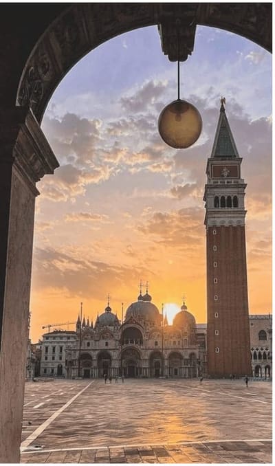 Piazza San Marco quasi deserta all'alba, la Basilica e il Campanile visti da sotto un portico