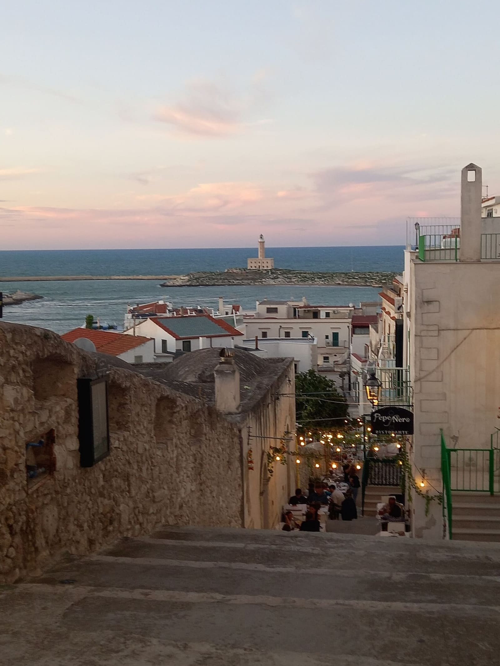 eine Treppe der Altstadt am Abend, mit den Tischen der Restaurants und dem Leuchtturm im Hintergrund